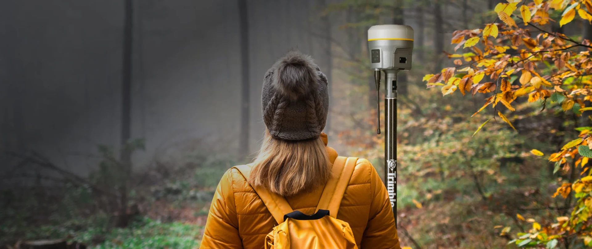 Surveyor facing forest carrying a Trimble R12i antenna