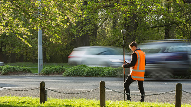Man on a road side using a trimble antenna to survey