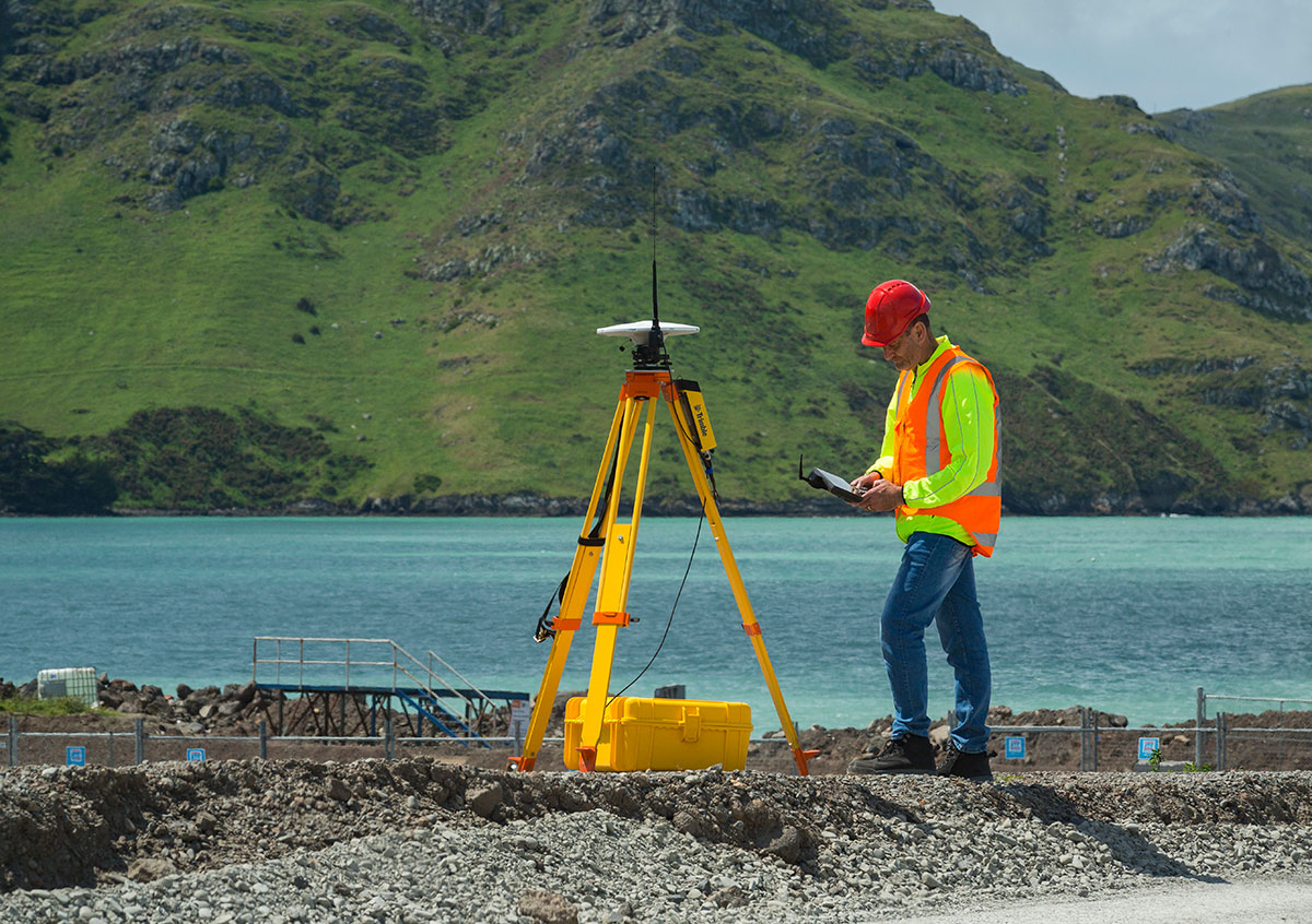 Worker with a Trimble GNSS receiver on a jobsite near a cove