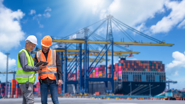 Two workers standing in front of a shipping container transport at a industry dock
