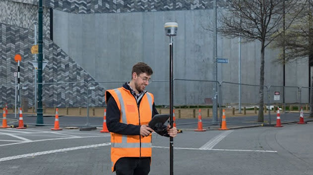Man standing on a street holding a trimble surveying antenna