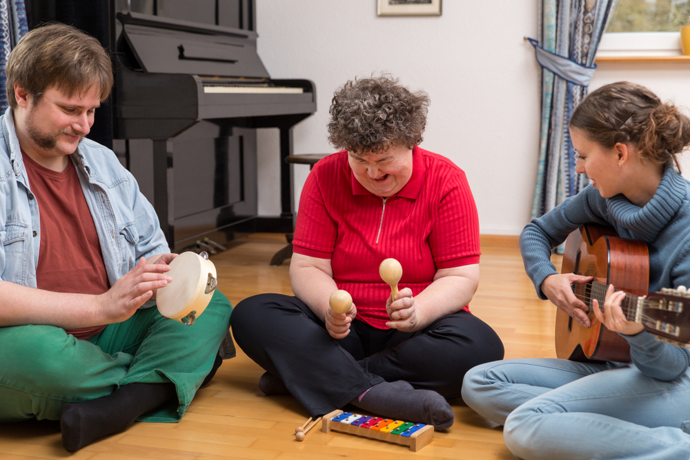 Three people sitting on the floor playing the guitar, maracas, and tambourine. 