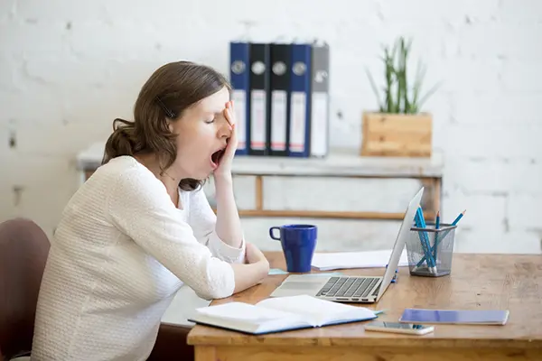 Woman sitting in front of her computer, yawning.