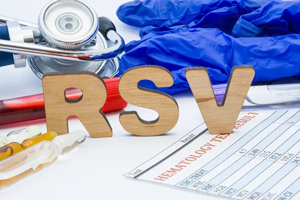 Wooden letters spelling RSV are standing up on a table. Also on the table is a stethoscope, rubber gloves, and a piece of paper that says Hematology Test Results.