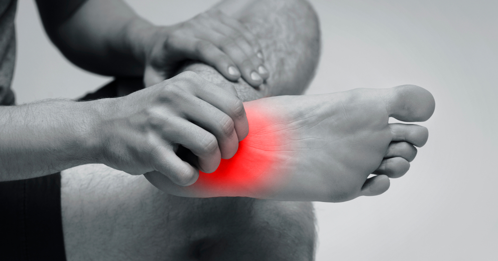 A man scratching an itch on the bottom of his foot. The area he's scratching is illuminated in a bright orange, signifying itchiness or pain. 