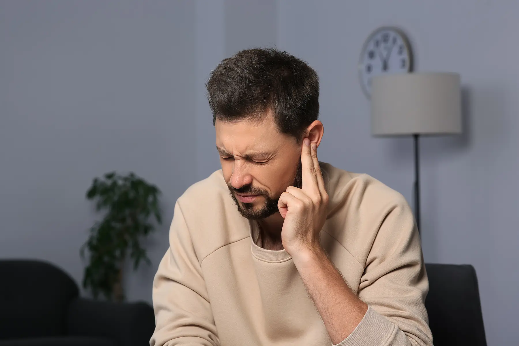 Man putting his fingers to his ear and wincing.