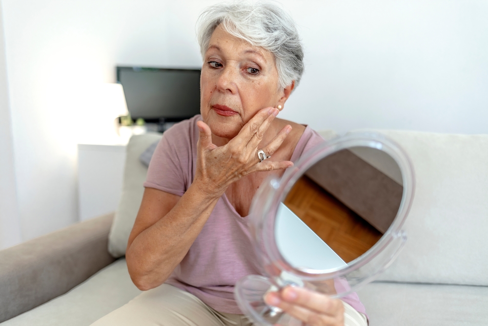 Older woman looking at her skin through with a hand mirror