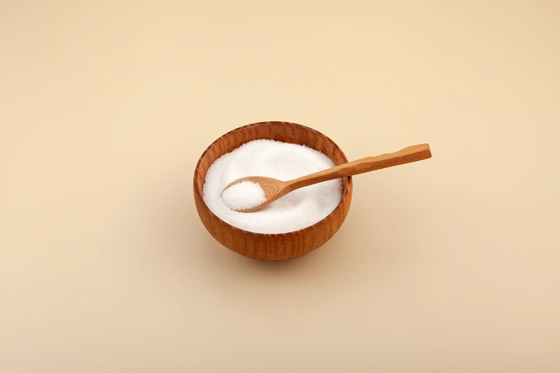 Wooden bowl of maltitol with a wooden spoon scooping some of it up.