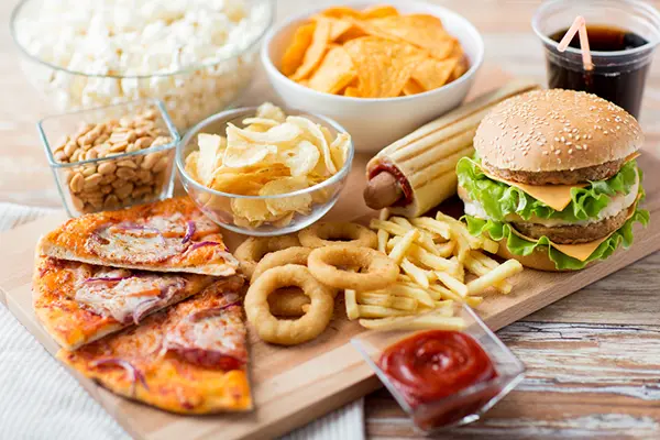 A collection of high-fat foods such as a cheeseburger, onion rings, French fries, pizza, and potato chips. 