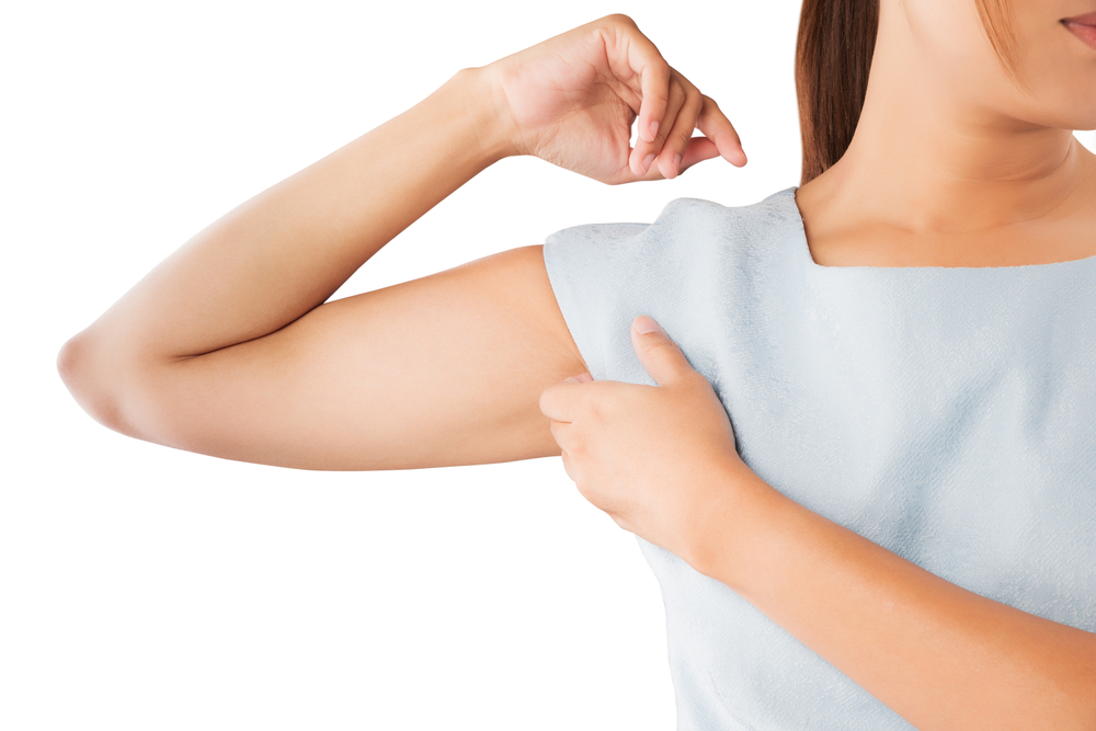 A woman in a blue tee shirt scratches her armpit.