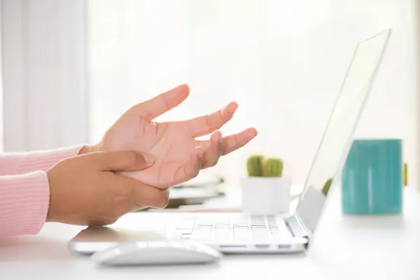 A person holds their hands in front of a computer screen.