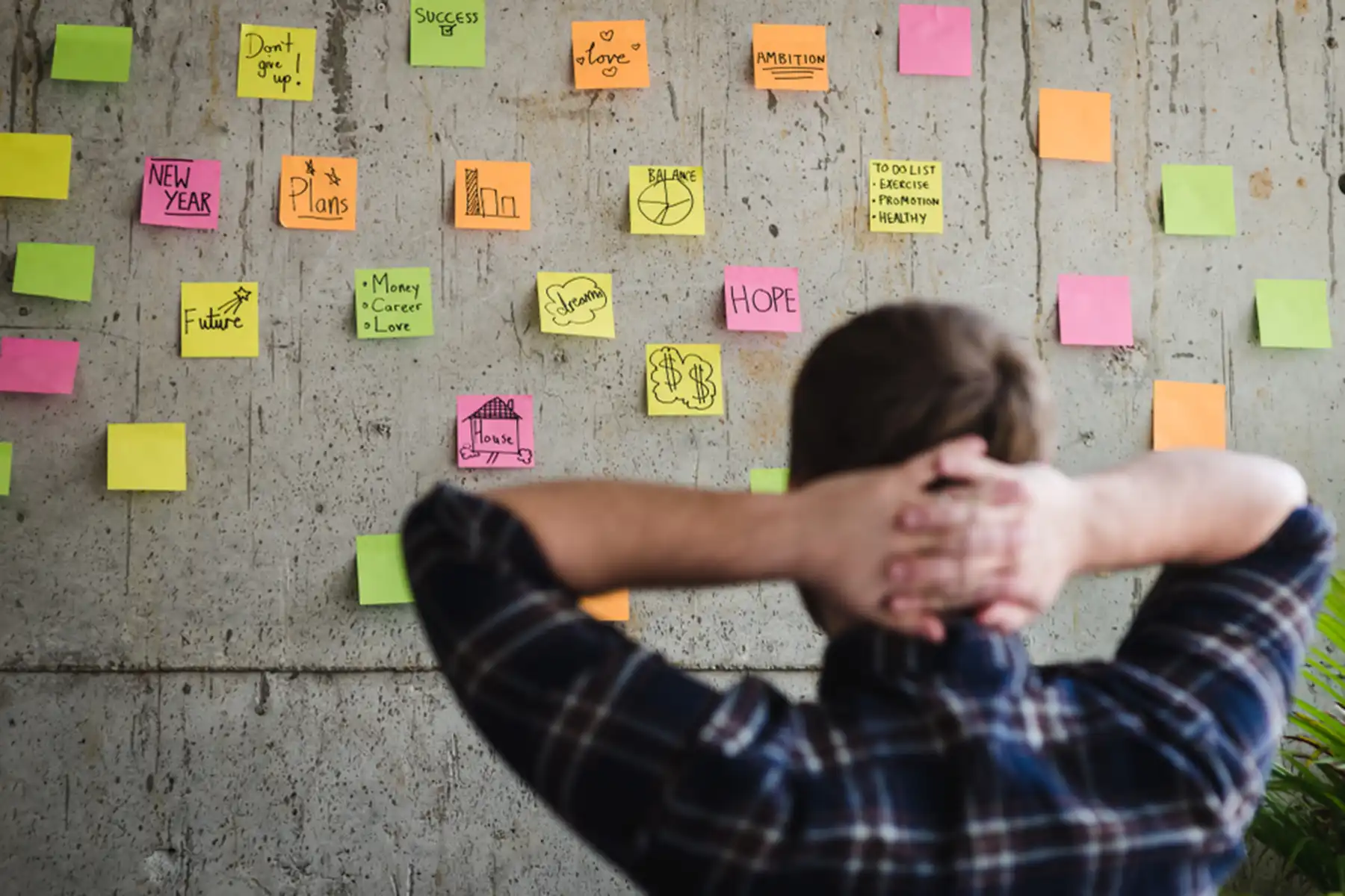 A man leans back in his chair and looks at sticky notes on a wall with ideas on it.