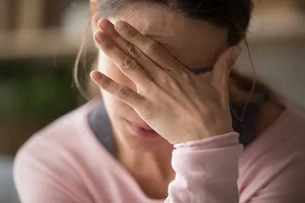 A woman in a pink long-sleeved shirt rests her head in her hand. She appears to be in discomfort. 