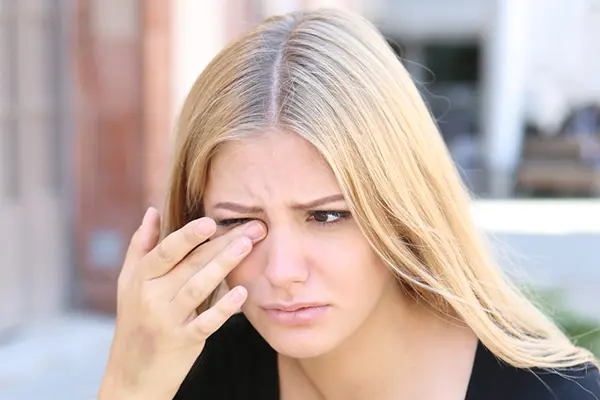 A woman itches her eye, making a pained face.