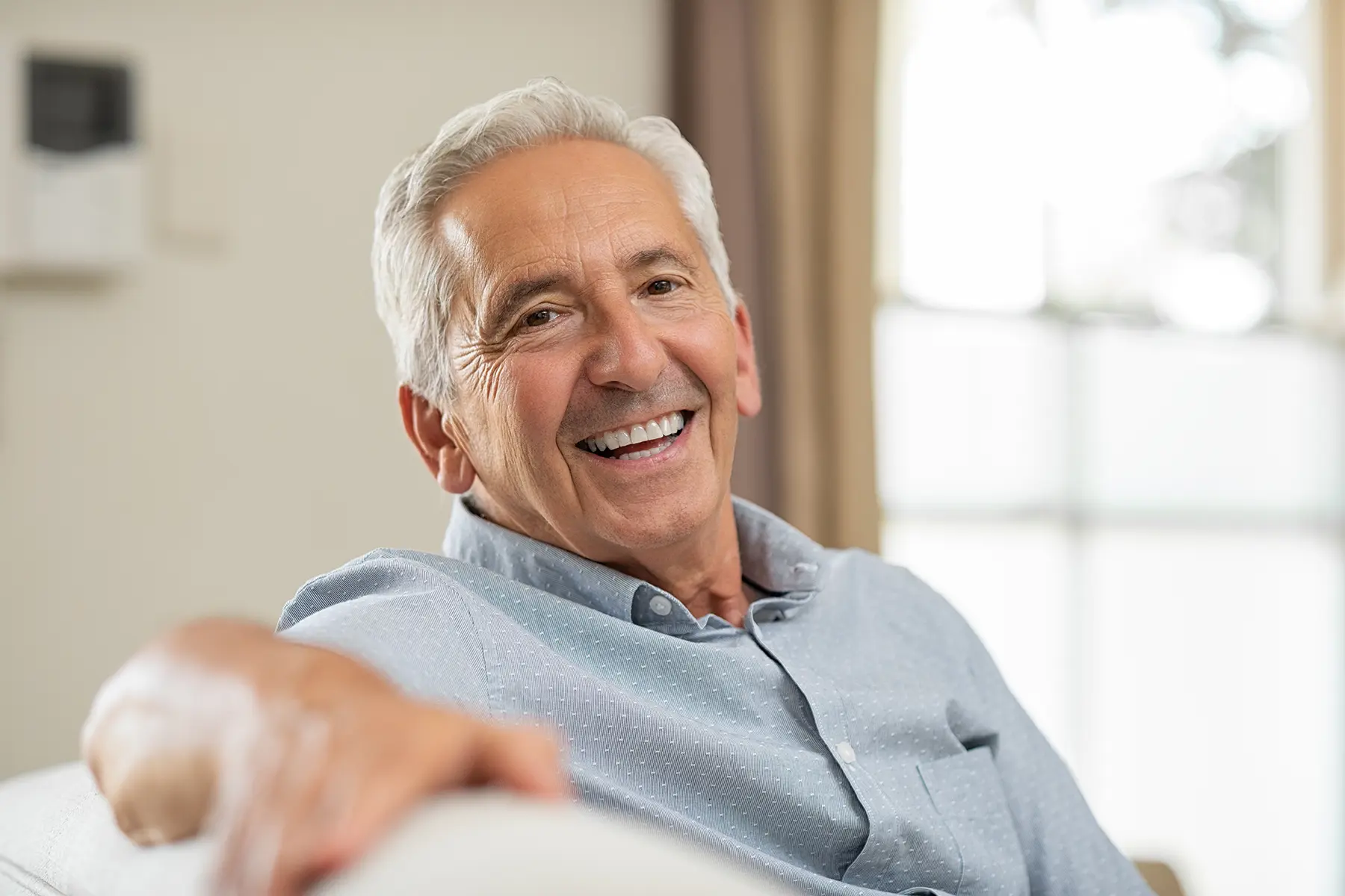 Older man sitting on the couch and smiling.