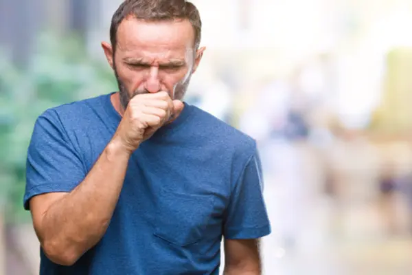 A man in a blue t-shirt coughing into his fist