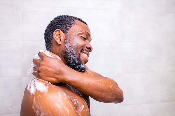 A man in the shower lathers up with a sponge and soap. 