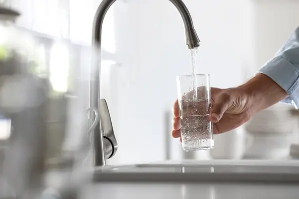 A hand holds a glass under a faucet of running water while the glass fills up with water. 