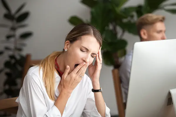 Woman sitting in front of a computer and yawning.
