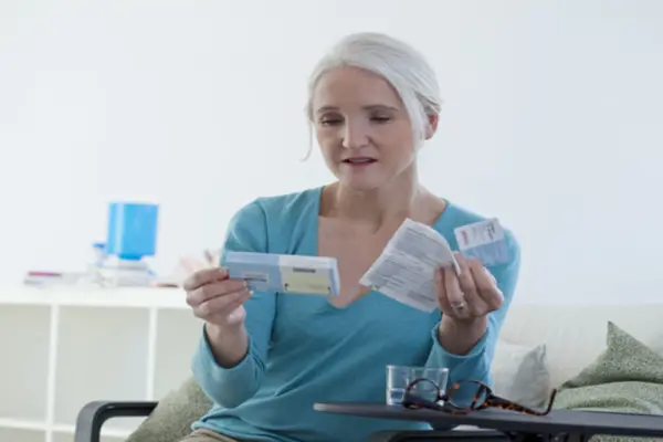 An older woman looking at a box of medication and holding instructions in the other hand