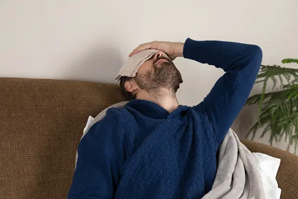 A man lays back on a couch and holds a compress over his eyes.