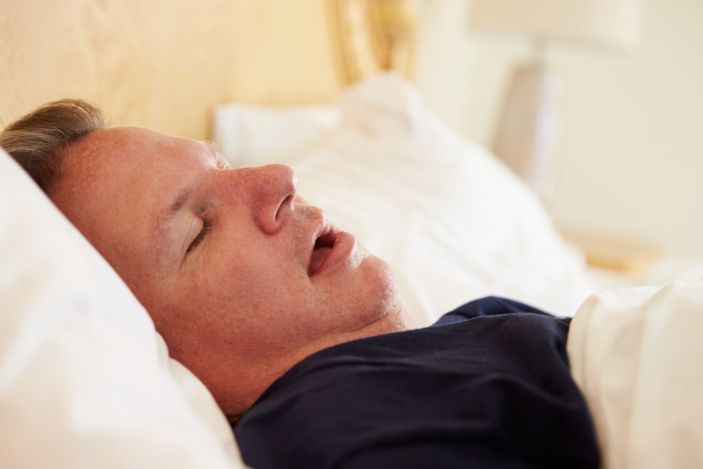 Close-up of a heavy-set man sleeping in bed with his mouth slightly open.