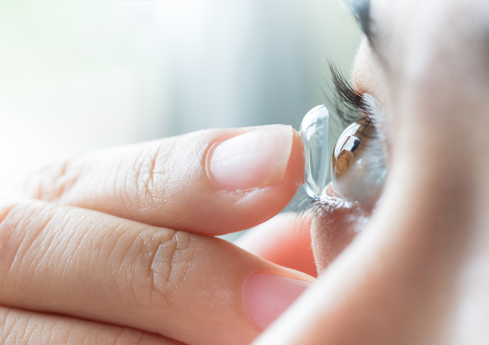 A close-up of a woman putting a contact lens into her right eye. 