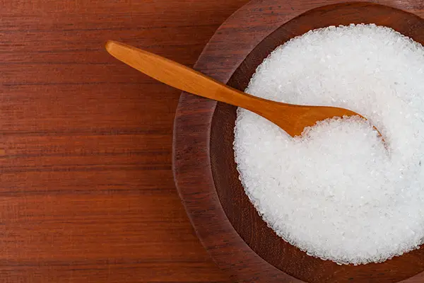 A wooden bowl of Magnesium Sulfate, also known as Epsom salts. There is wooden spoon resting in the salts. 