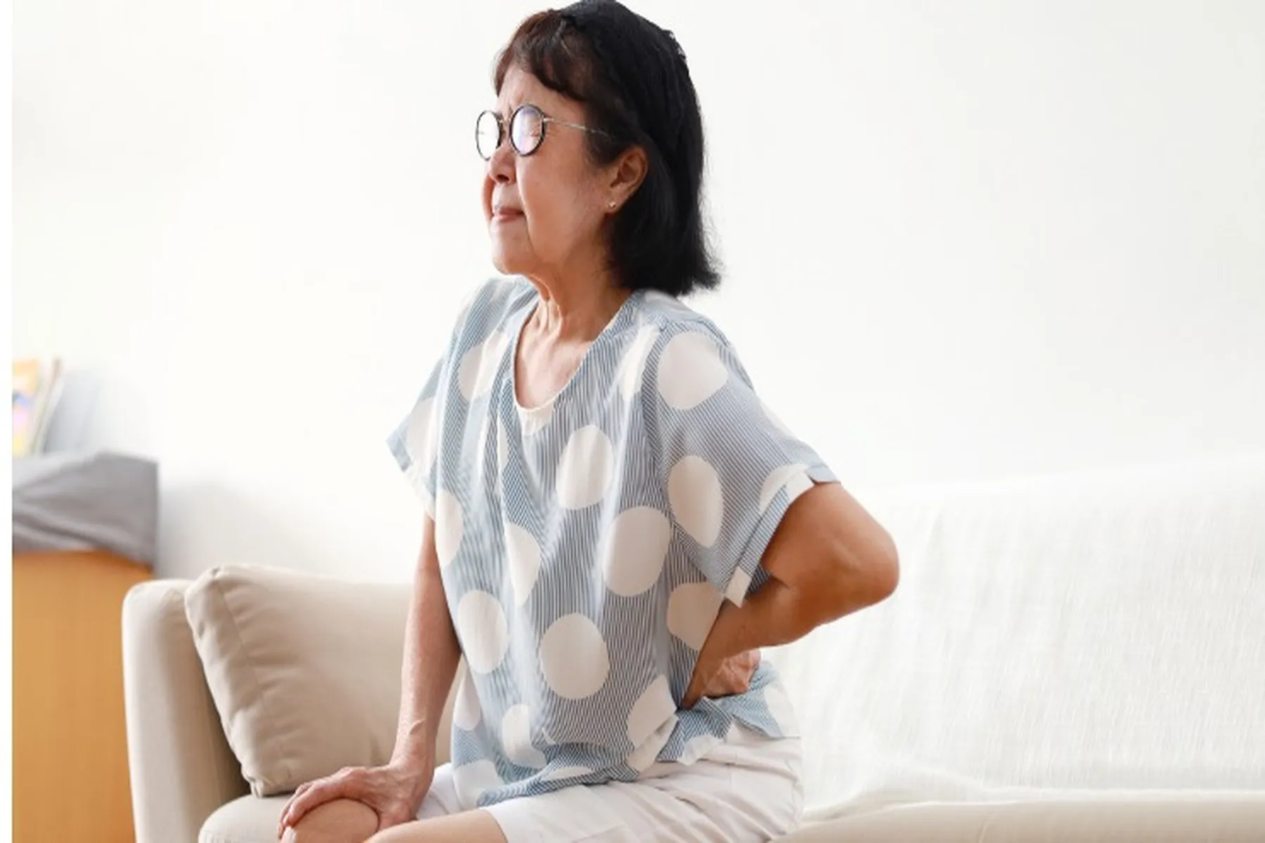 Older woman sitting on couch holding her joints and grimacing.