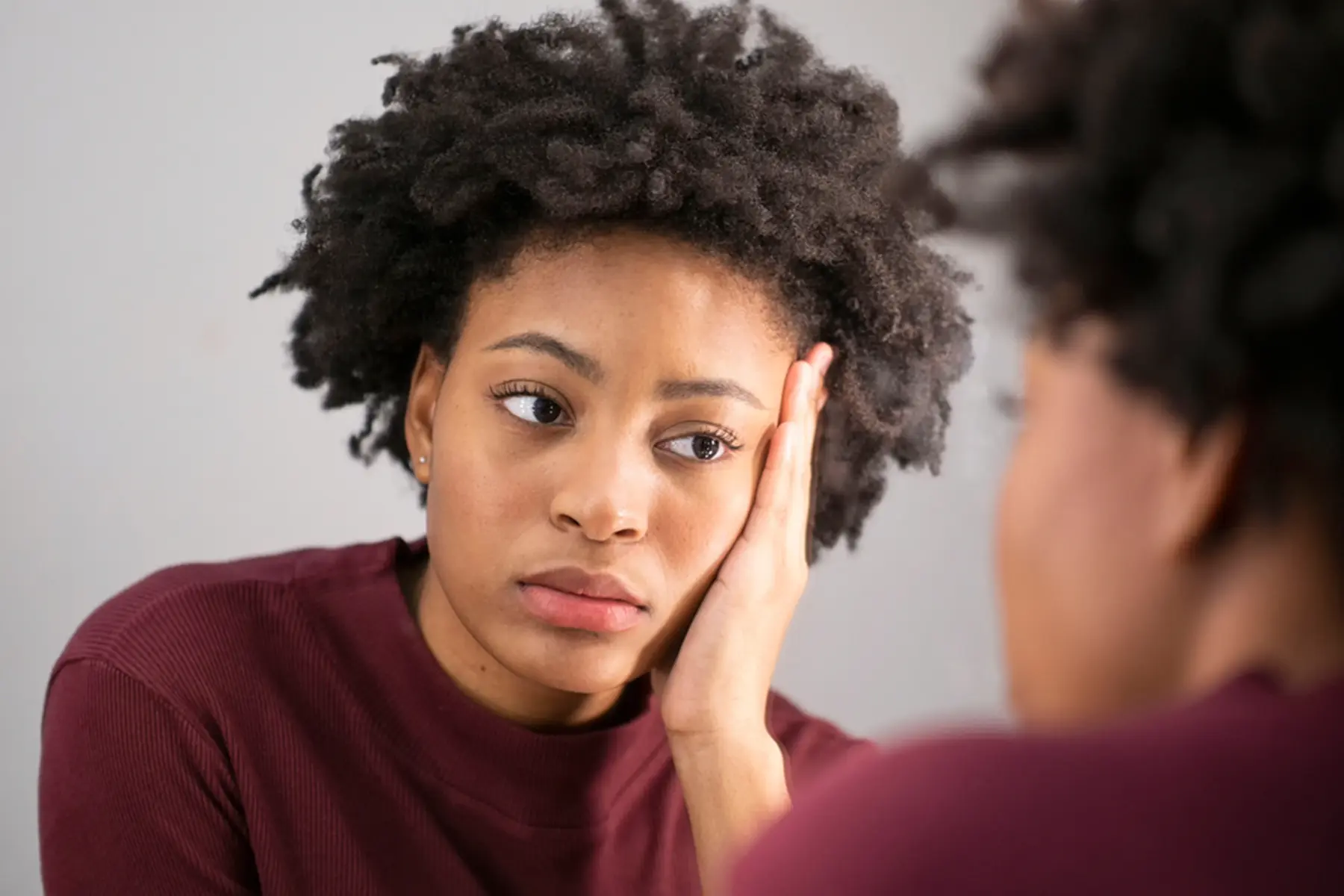 A woman looks at herself in the mirror and makes a depressed face.