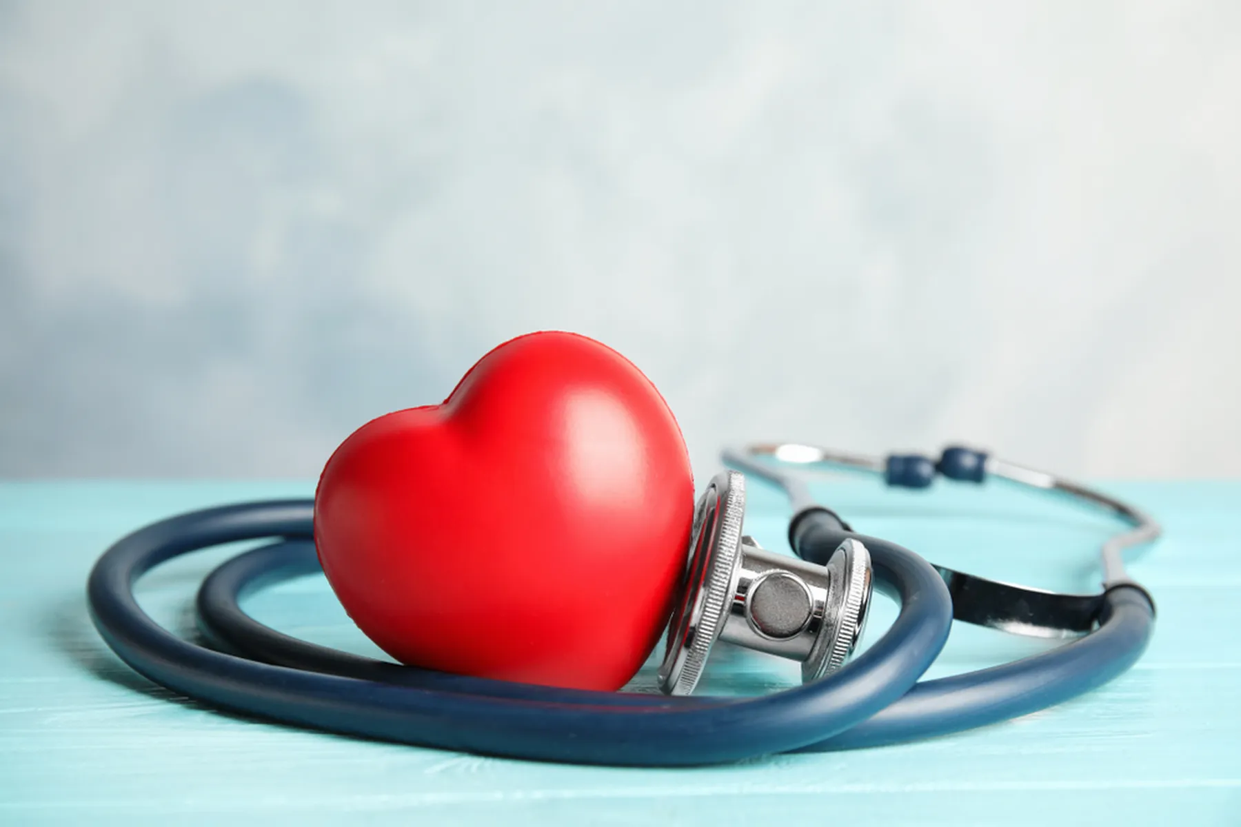 A red heart and a stethoscope sit on a light blue wooden table. 