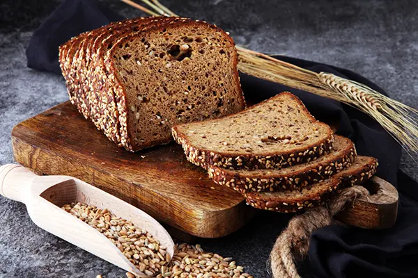 A loaf of whole grain bread with wheat stocks and grains around it.