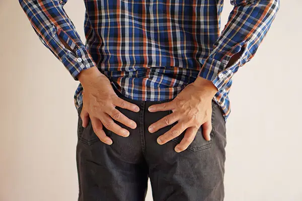 A man in a flannel shirt with his hands on his buttocks.
