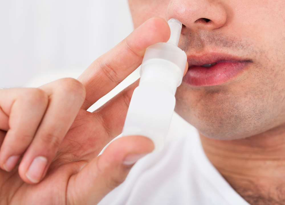 A man uses a nasal spray in his nostril.