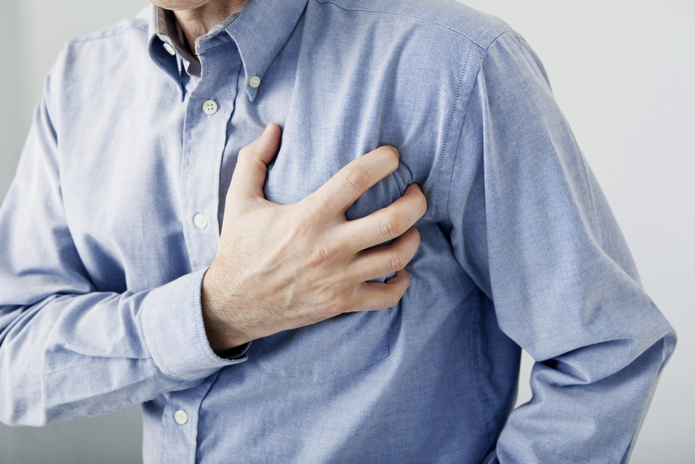A close-up of a man's right hand clutching the right side of his chest. The photo signifies he may be having a heart attack. 