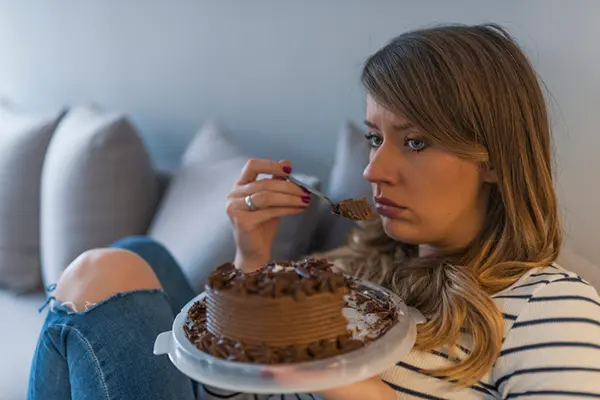 A woman sits crying and eats a forkful of chocolate cake.