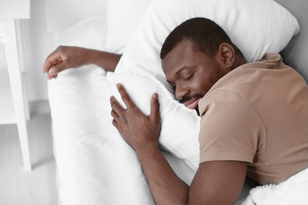 A man lays on his sides in bed and sleeps peacefully.