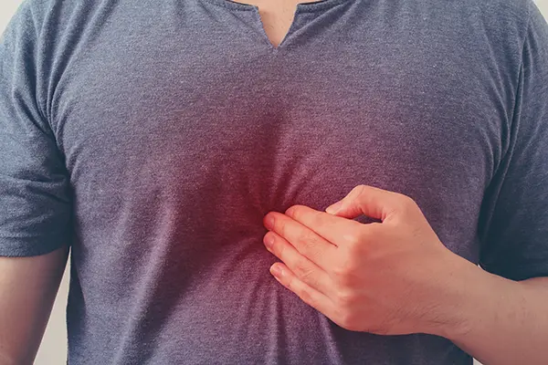 A man holds the tips of his fingers to the area under his breastbone. He is likely suffering from heartburn or GERD.