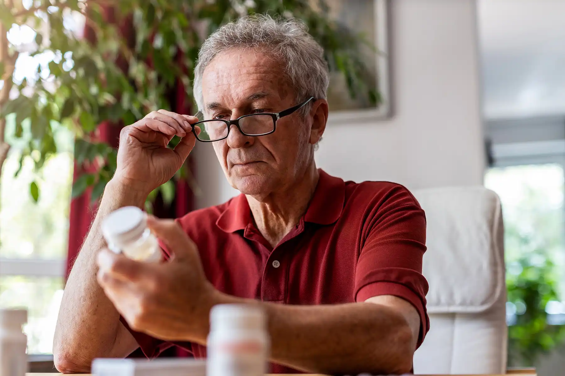 Older man putting on his glasses to read the label of his prescription pill bottle.