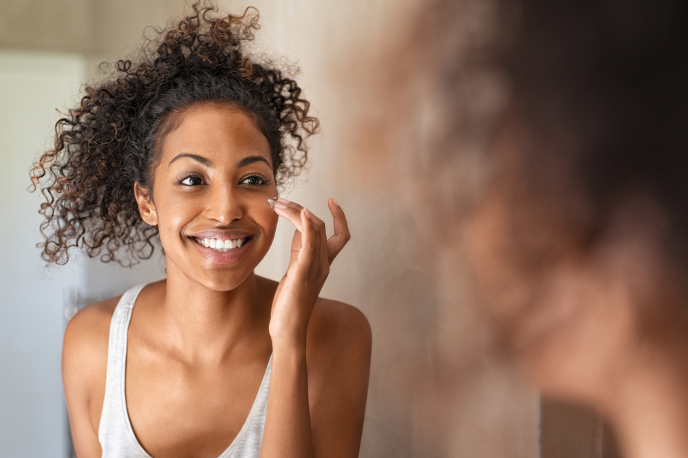 Woman looking in mirror and putting cream on her face.