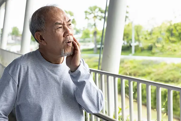 A man stands outside and holds the side of his face in pain.