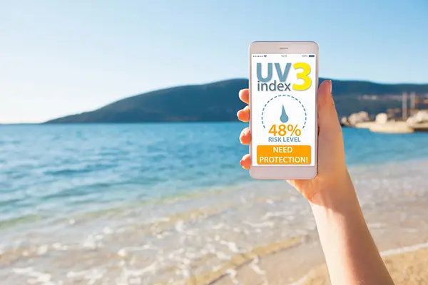 Someone holding a phone at the beach and looking at the UV index.