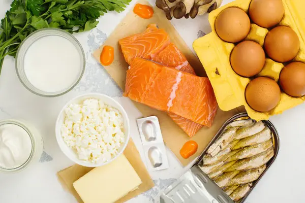 A glass of milk, fatty fish, cheese, eggs and other foods that are rich in vitamin D on a counter.