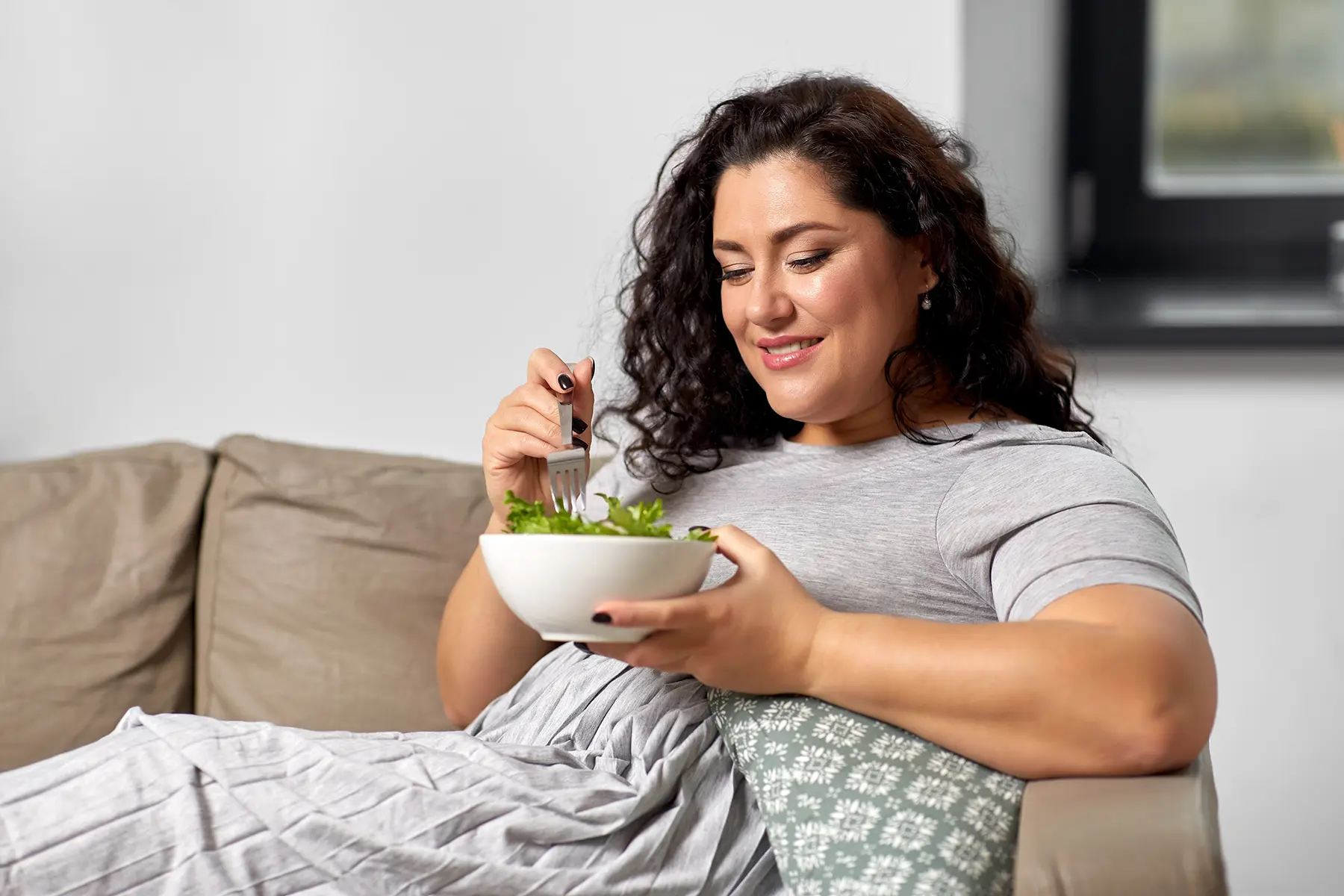 Woman sitting on her couch eating a salad.