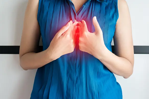A woman holds her hands between her breastbone. She is presumably suffer from symptoms of heartburn, acid reflux, or GERD. 
