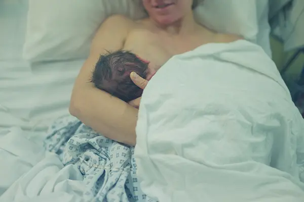 A woman lays in a hospital bed and holds her newborn baby.
