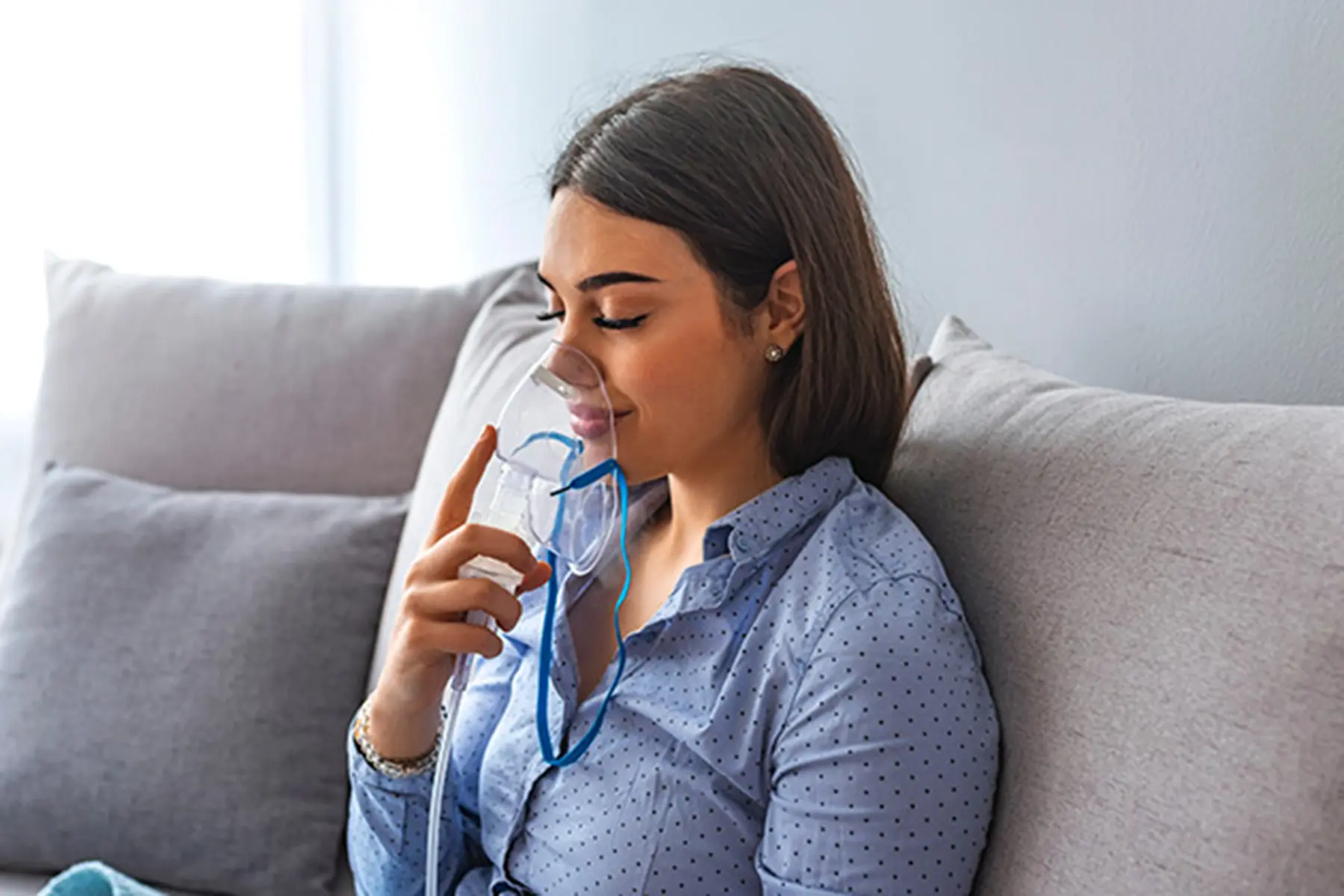 Woman sitting on her couch and breathing into her nebulizer.