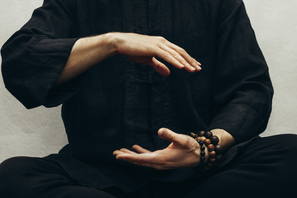 Man sitting in a traditional tai chi position with his arm in front of him in a circular position.