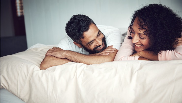 A man and a woman are laying in bed together and laughing. 