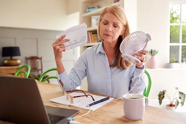 Woman holds mini fan up to her face while having a hot flash.